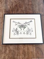 Framed Inuit artwork print featuring birds and fish in monochrome with green highlights, placed on wooden surface