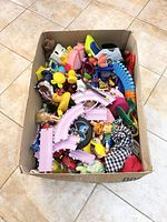 Photo of large cardboard box filled with mixed children's toys including toy train tracks, rubber ducks, stuffed animals and vehicles