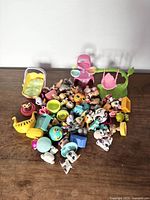 Overview of Littlest Pet Shop figures and accessories scattered on a wooden surface showing variety of animals, furniture pieces, and play items.