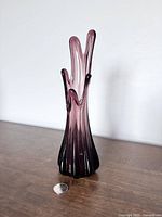 Front view of the purple five finger swung glass vase on a wooden surface with a coin for scale.