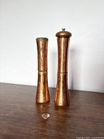 Front view of the vintage copper salt shaker and pepper grinder showing their shape and height difference with a coin for scale.