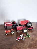 Photo showing six vintage diecast toy tractors arranged on a white surface from a front angle, displaying colors and sizes.