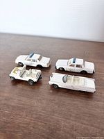 Top-down view showing all four white ERTL Dukes of Hazzard toy cars in varying conditions on a wooden surface