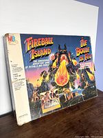 Photo showing worn vintage Fireball Island board game box with colorful volcano and adventurer artwork, box edge damage visible