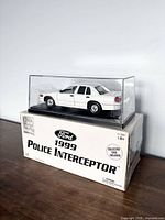 Front and side view of the diecast Ford Police Interceptor model in clear plastic case on original box showing branding and collector scale info.
