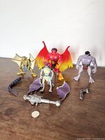 Group shot showing all three Gargoyles figures and scattered accessories on a wooden surface with a white background.