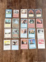 Photo showing 20 assorted Magic The Gathering cards spread out on wood surface with various fantasy characters and spells depicted in various colors.