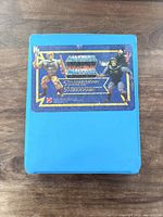 Exterior of blue carrying case with sticker showing 5th anniversary Masters of the Universe graphics, featuring He-Man and Skeletor characters.