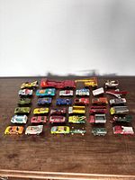 Photo of 29 vintage diecast toy vehicles laid out on wood surface showing variety of models including cars, trucks, bus, plane and locomotive.