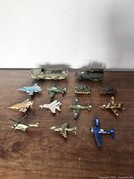 Overview of all 14 vintage military toy vehicles and airplanes arranged on wood surface.