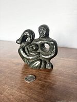 Front view of the abstract modernist sculpture, showing intertwined human forms and signed by Edmund Sharp. Placed on a wooden surface with a quarter coin for scale.