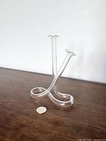 Clear vintage glass test tube propagation vase displayed on wooden surface with coin for scale, showing side angle with two vertical tubes and rounded base