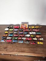 Wide view of the full collection of vintage toy cars and vehicles laid out on a wooden surface, showing quantity and variety.