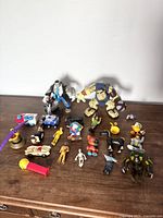 Overview of assorted vintage toys and action figures arranged on a flat surface including vehicles, humanoid characters, and animal figures.