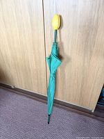Full view of the closed umbrella showing the green fabric and tall yellow tulip handle at the top.