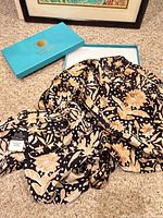 Black and tan floral silk scarf spread out beside Smithsonian teal box