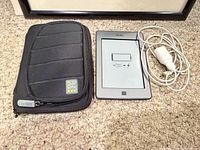 Kindle e-reader, case, and charger laid out on carpet