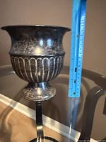 Full view of metal urn vase beside ruler showing height
