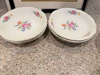 Stack of six white ceramic bowls with floral decals and scalloped worn rims
