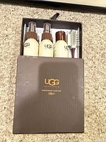 Closed brown UGG box pulled halfway to show three beige bottles and white brush inside