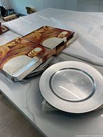 Set of silver charger plates partially visible in original packaging on a table.