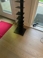 Front angled view of the black metal vertical shelf tower with multiple square shelves and wide base.