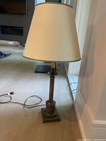 Full view of brass table lamp on wooden floor against wall, showing overall shape and base details.