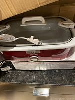 Photo of the red and white Crock-Pot slow cooker unit with glass lock lid and power cord visible.