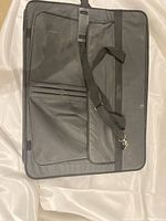 Full view of the black nylon artist bag lying flat, showing front exterior compartments, handles, and attached shoulder strap.