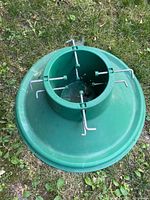 Top view of green plastic Christmas tree stand showing central cylindrical holder and metal tightening screws.