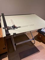 Front view of the full-size drafting table showing white work surface with parallel ruler and adjustable protractor tool.