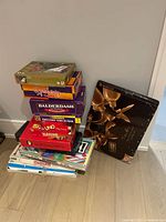 Photograph of stacked assorted board and card games with clear box titles: Speakeasy, Balderdash, Menza, Uno, Yahtzee, Scattergories, Sorry, Monopoly, Easy Money, Pictionary, painting, and jigsaw puzzle included.