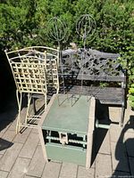 Photo showing garden bench, hose reel storage, iron chairs, small iron table, and two iron spherical topiary forms against greenery background