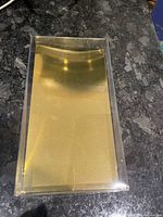 Clear rectangular plastic box showing the gold paper lining at the base, closed with lid.