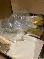 Plastic wrapped gold lined bases and clear gift boxes in a cardboard box.