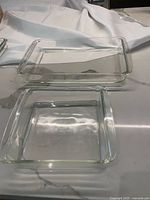 Two Pyrex glass baking dishes, one rectangular 9x13 inch and one square 8x8 inch, placed on a flat surface with white cloth background.