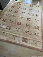 Full view of carpet laid on wood floor showing beige background with grey and brown floral and geometric designs in tiled pattern with border.