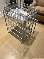 Unassembled stack of 8 metal wire baskets with rectangular shapes and wire mesh base, showing a partially assembled frame supporting one basket.