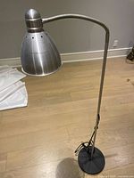 Full view of the IKEA LISSTA metal floor lamp showing silver adjustable lamp head, flexible arm, and black base on wood floor.