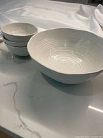 Set of one large white ceramic bowl and three smaller matching bowls stacked, placed on white countertop.