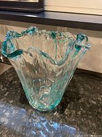 Green glass vase with wavy ruffled edges and textured glass body, placed on a dark granite countertop.