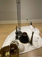 Overview of the lighting lot on floor including two brass table lamps, floor lamp, lampshade, and ceiling light globes on white fabric.