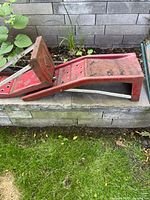 Side view of one red steel car ramp with visible rust and structural metal rods underneath for support.