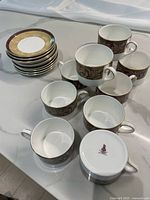 Ten bone china cups arranged on countertop with matching saucers stacked