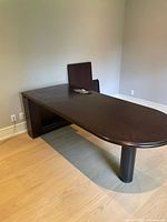 Photo of large cherry wood desk with rounded edge and dark finish, showing mixed leg base and clean surface.