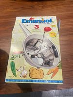 Photo of the original box of the Emanuel food mill showing the kitchen tool and colorful vegetable illustrations.