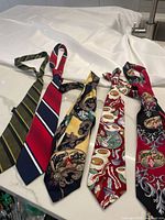 Four ties displayed on white cloth showing detailed patterns and logos
