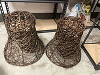 Two handcrafted bell-shaped decorations woven from grapevines on concrete floor, brown lattice natural wood texture, about 19 inches diameter and tall, open weave structure