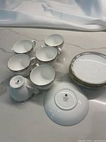 Six white bone china Wedgwood teacups with silver/platinum borders and matching saucers arranged on white surface.
