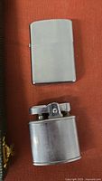 Two vintage metal lighters, one rectangular Zippo lighter with smooth chrome finish and one cylindrical Magna lighter with top igniter.